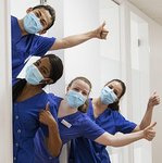 Vier PZR-Kräfte mit Mundschutz schauen mit Daumen hoch aus einer Tür heraus