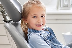 Blondes M&auml;dchen sitzt auf einem hellgrauen Zahnarztstuhl und l&auml;chelt in die Kamera (Hinweis: Bild ist KI-generiert)