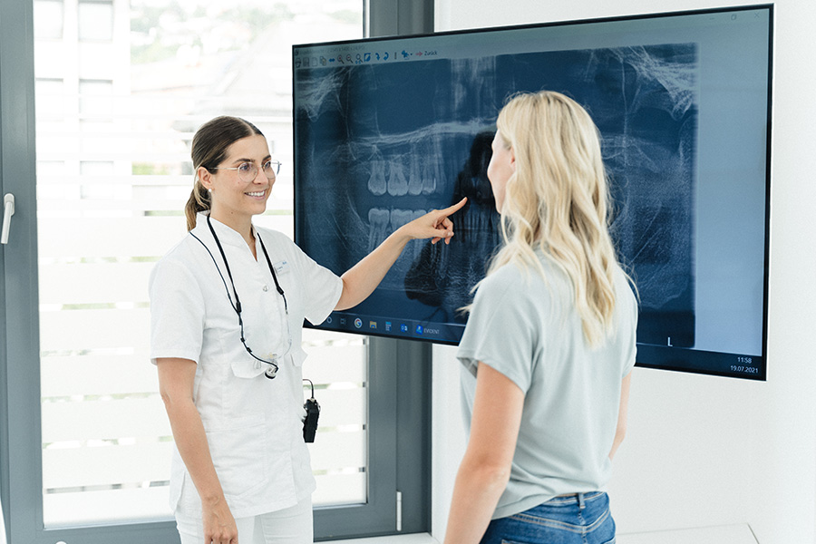 &Auml;rztin und Patientin schauen R&ouml;ntgenbild auf einem gro&szlig;en Bildschirm an