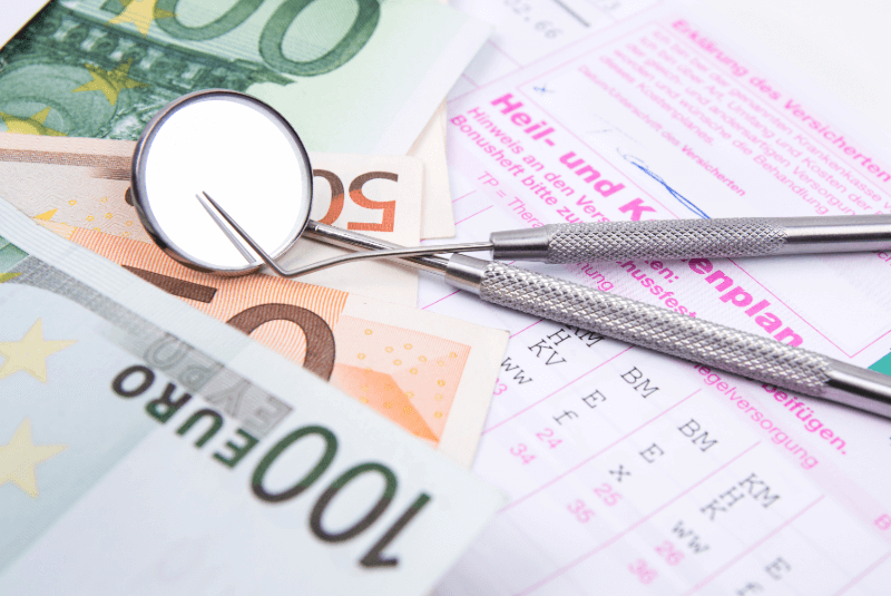 Nahaufnahme eines Zahnspiegels, der auf Geldscheinen und einem HKP liegt