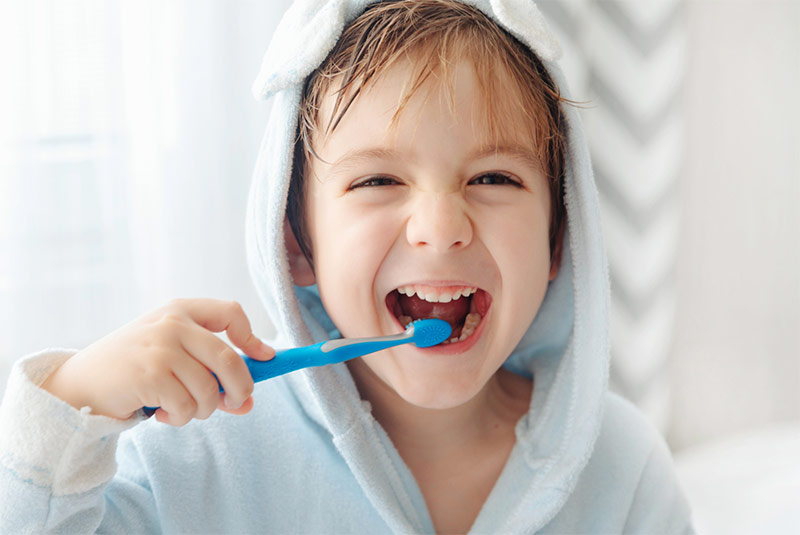 Junge in Bademantel putzt sich mit blauer Zahnbürste die Zähne
