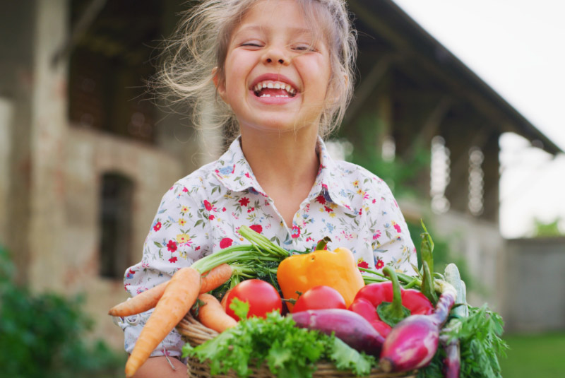 Blones Mädchen hält lachend einen Gemüsekorb fest
