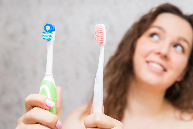 Frau Hält elektrische Zahnbürste in der rechten, Handzahnbürste in der linken Hand