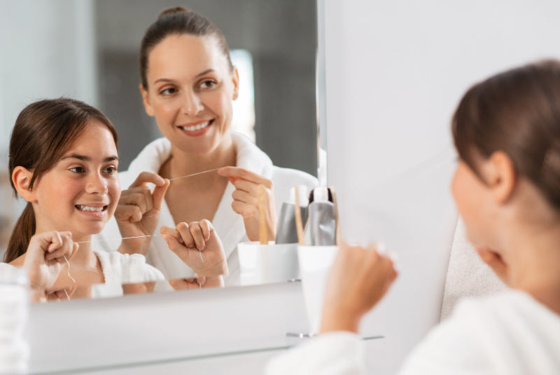 Mutter und Tochter stehenmit Zahnseide in der Hand vor dem Spiegel